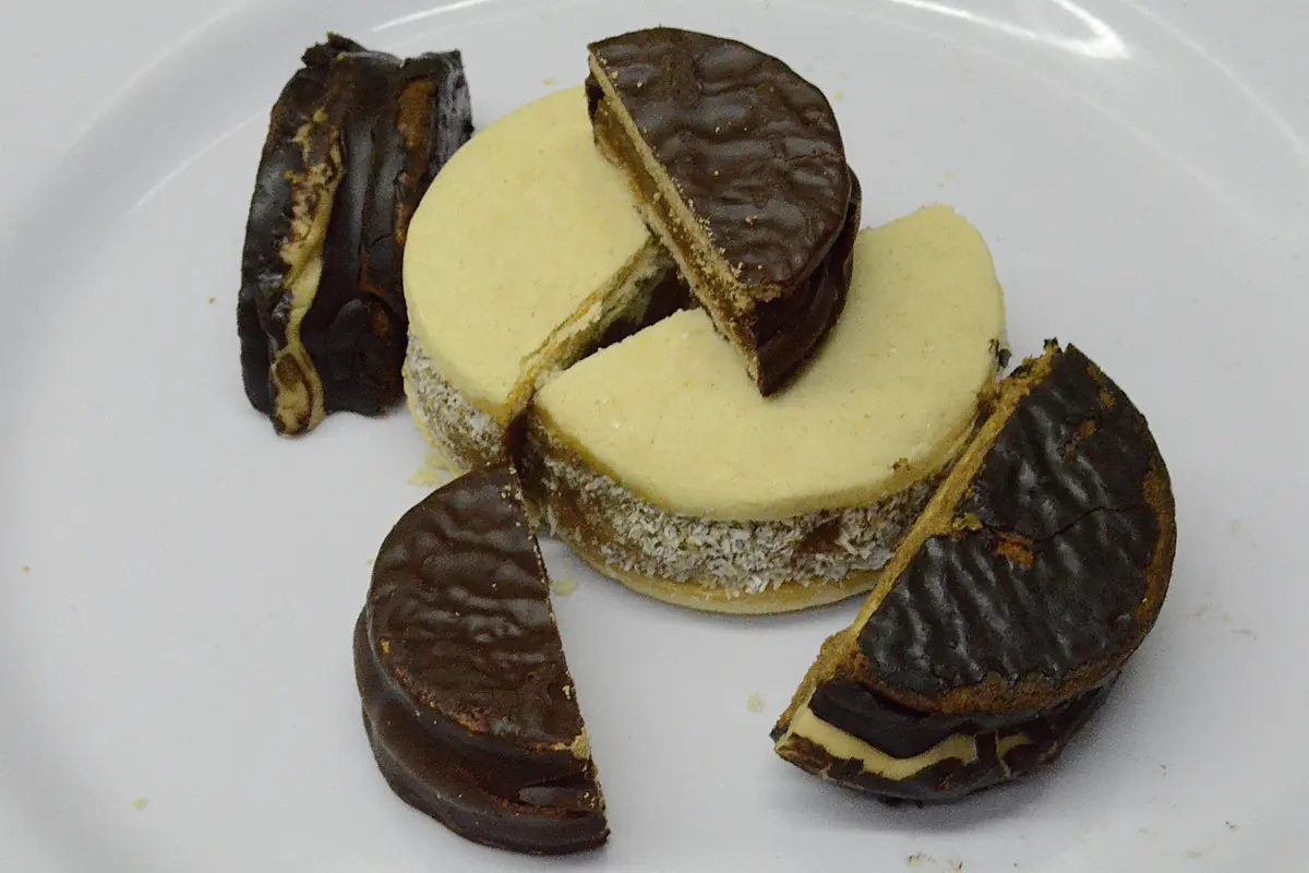Argentine alfajores on a white plate, chocolate-coated and white-glazed, one cut open to show the filling