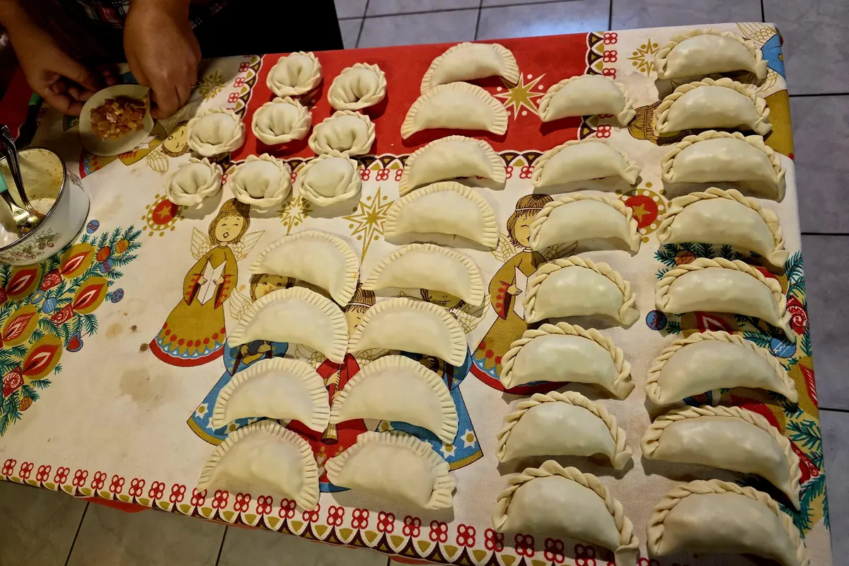 A family table covered in raw Argentine empanadas, each closed with a different braided or forked crimp